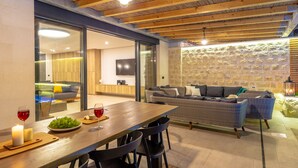 A modern interior with a dining area, wicker furniture, stone wall, and a television in the background. - Hedera Estate, Villa Hedera II (Dubrovnik)