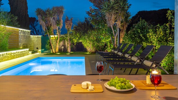 An outdoor pool area with lounge chairs, a table with cheese and grapes, and a glass of red wine. - Hedera Estate, Villa Hedera II (Dubrovnik)
