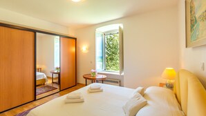 A bedroom with a bed, a nightstand, a window with a view, a radiator, and a sliding door. - Hedera Estate, House Hedera V (Dubrovnik)