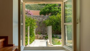 A view through an open door into a garden with a stone wall, a wooden bench, and a clear sky. - Hedera Estate, House Hedera V (Dubrovnik)