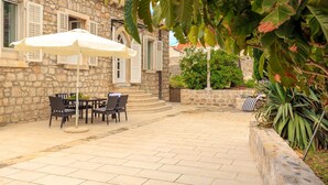 A stone building with a patio area featuring a table and chairs under a white umbrella. - Hedera Estate, House Hedera V (Dubrovnik)