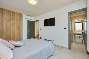 A bedroom with a bed, a wooden wardrobe, a TV, and a bathroom visible through an open door. - Hedera Estate, Villa Hedera (Dubrovnik)