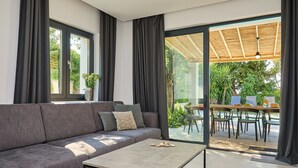 Un salon moderne avec un canapé gris, une table basse et une porte vitrée donnant sur un espace repas extérieur.