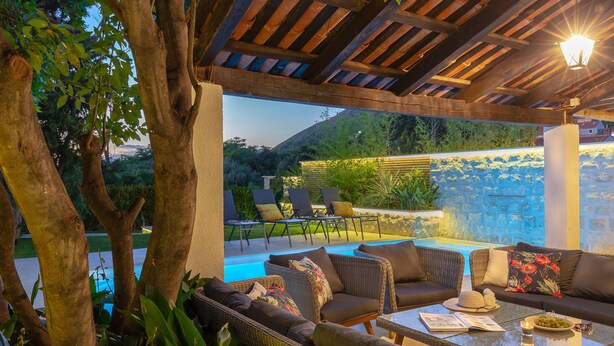 Une terrasse extérieure avec des meubles en osier, une piscine et un mur en pierre.