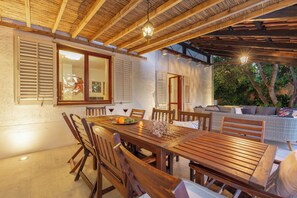 An outdoor dining area with wooden tables and chairs, a wicker sofa, and a pergola with hanging lights. - Hedera Estate, Villa Hedera (Dubrovnik)