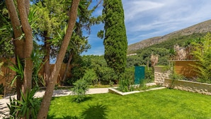 Un jardin bien entretenu, agrémenté de divers arbres et arbustes, d’un mur en pierre et offrant une vue dégagée sur un paysage vallonné en arrière-plan.