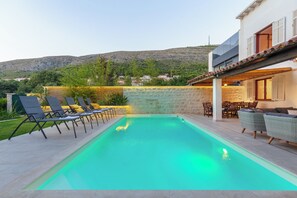 A swimming pool with lounge chairs, a stone wall, and a view of a hillside. - Hedera Estate, Villa Hedera (Dubrovnik)