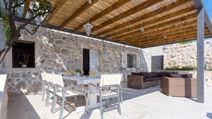 Un bâtiment en pierre doté d’un patio couvert, d’un espace extérieur aménagé avec des sièges et d’une table avec des chaises.