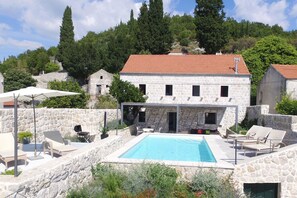 A stone building with a swimming pool, outdoor seating, and a view of a forested hillside. - Hedera Estate, Villa Hedera Viii (Dubrovnik)