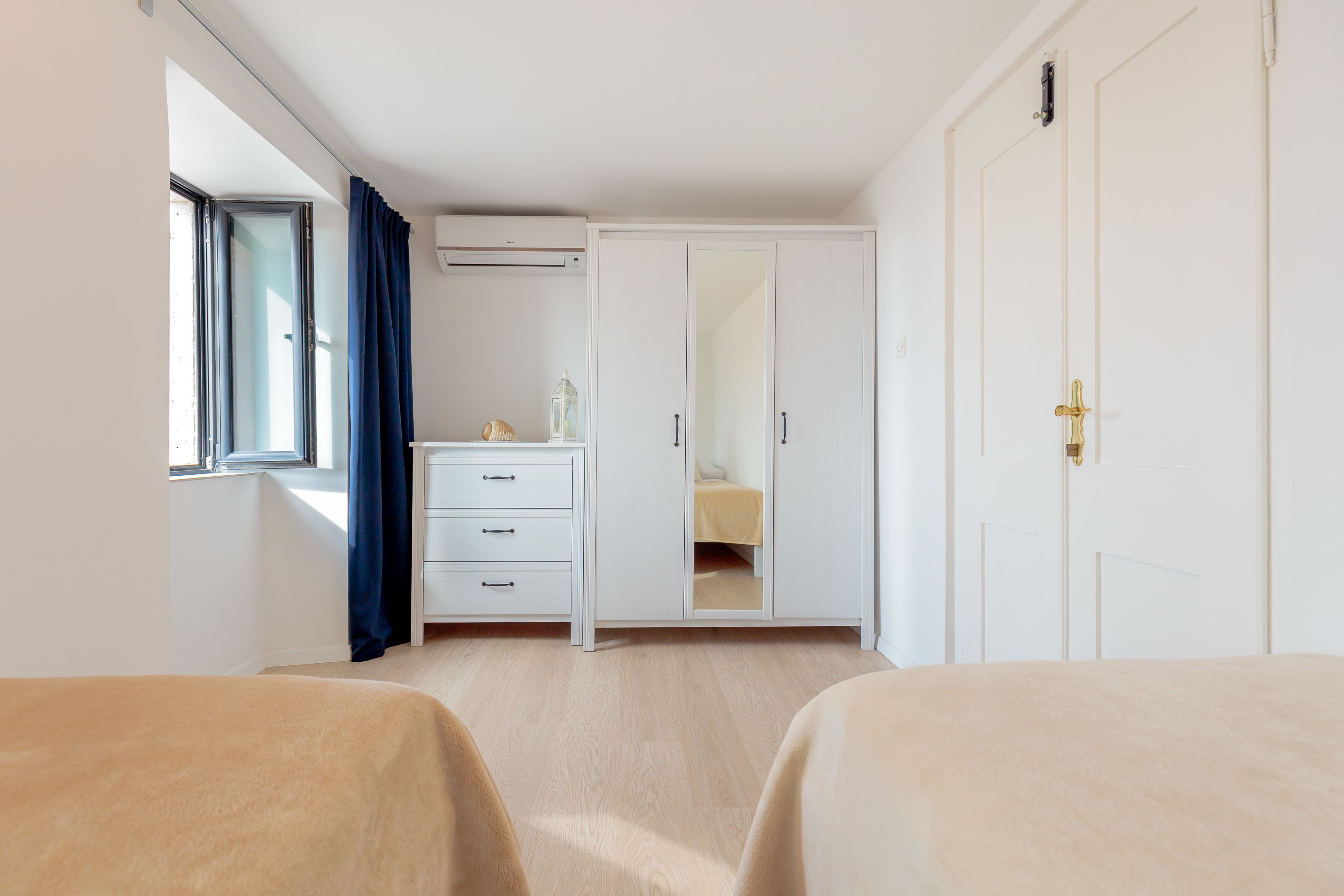 A bedroom with two beds, a wardrobe, a mirror, and a window with curtains.