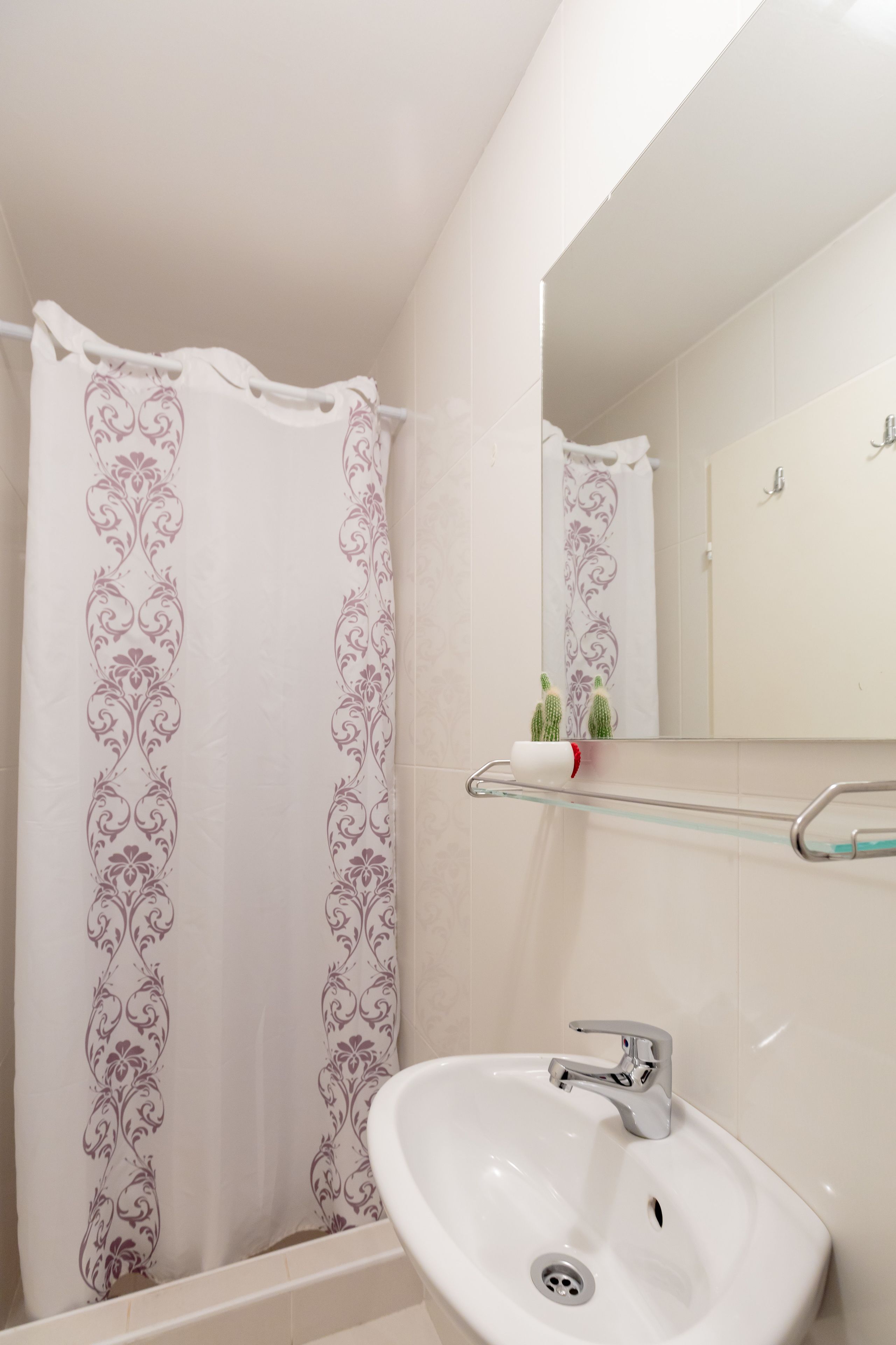 Un baño con cortina de ducha, lavamanos y espejo.