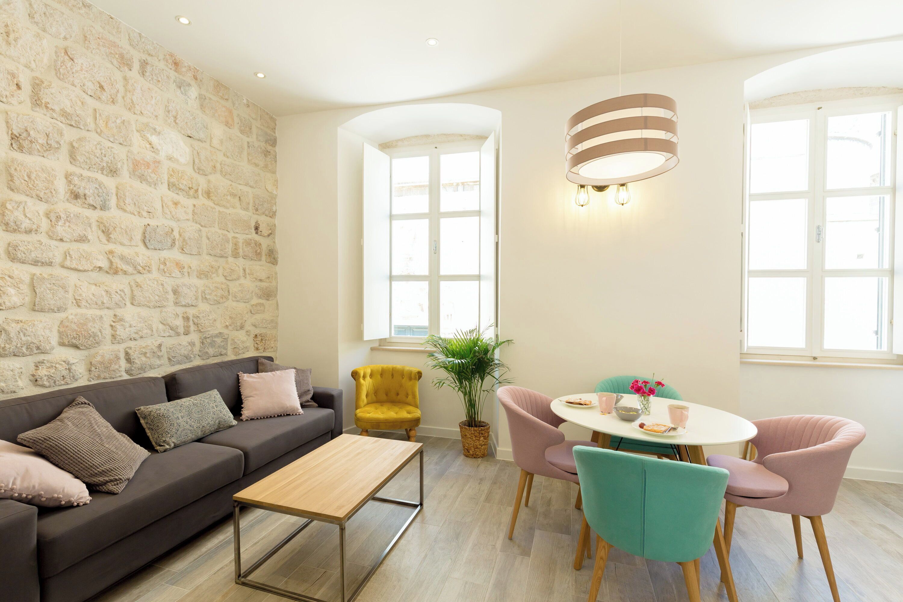A modern living room with a stone wall, a sofa, a dining table with chairs, and a hanging light fixture.