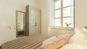 A bedroom with a bed, a wardrobe, a mirror, a window with a view, and a vase with flowers. - Hedera Estate, Hedera A2 Apartment (Dubrovnik)