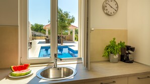 Una cocina con un lavamanos de acero inoxidable, un reloj en la pared, una planta en maceta y vistas a una piscina exterior.