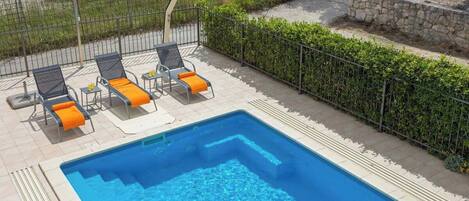 Une piscine rectangulaire, bordée d’un revêtement de carrelage, entourée d’une clôture en métal et d’une haie.