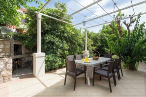 Eine Terrrasse im Freien mit Tisch und Stühlen, umgeben von Grünpflanzen und einer Pergola.