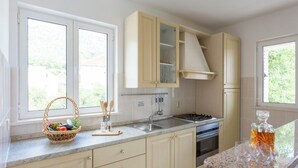 A kitchen with a granite countertop, wooden cabinets, a stainless steel sink, and a window with a view of greenery. - Villa Florence - Mediterranean Garden&pool (Dubrovnik)