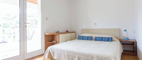 A bedroom with a bed, a nightstand, a desk, and a sliding glass door to the outside.