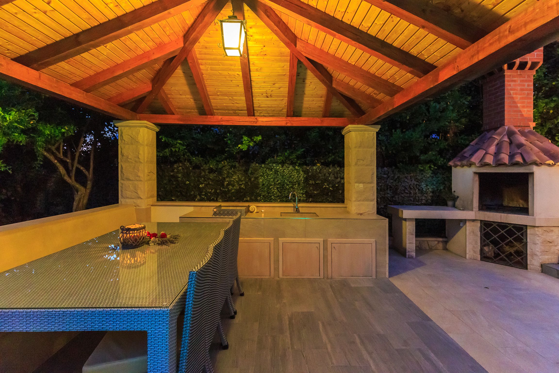 An outdoor kitchen area with a pergola roof, a stone chimney, and a built-in grill.