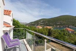 A balcony with a glass railing overlooking a hillside with houses and a body of water. - Hedera Estate, Villa Hedera X (Dubrovnik)