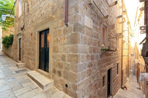 Un estrecho edificio de piedra con una puerta negra, un ventanal pequeño y una escalera que lleva a la entrada.