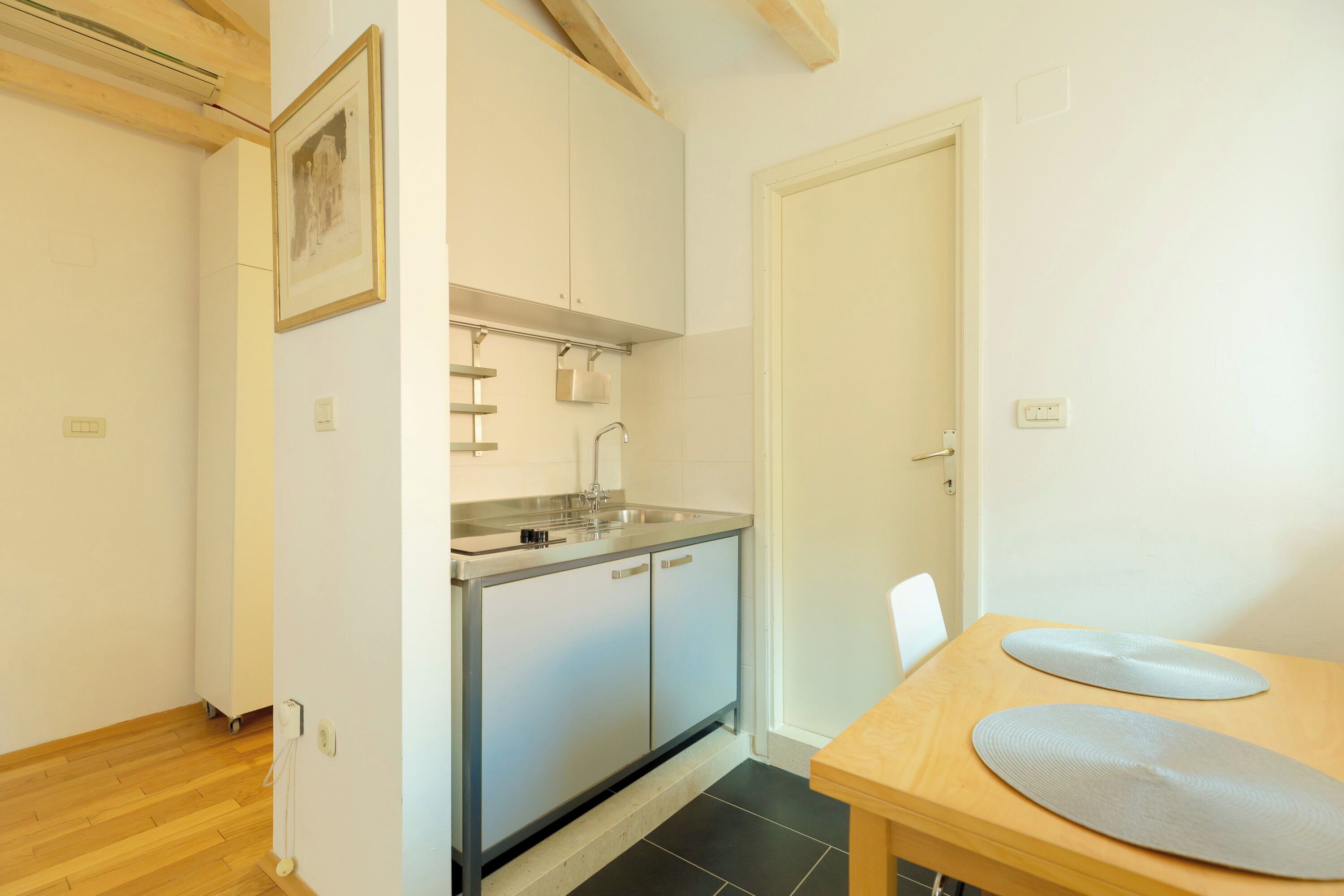 A small kitchen with a sink, cabinets, and a dining area with a table and chairs.