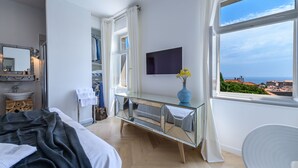 A modern bedroom with a bed, a vanity with a mirror, a dresser, and a large window offering a view of the sea. - Villa Donna Paola (Dubrovnik)