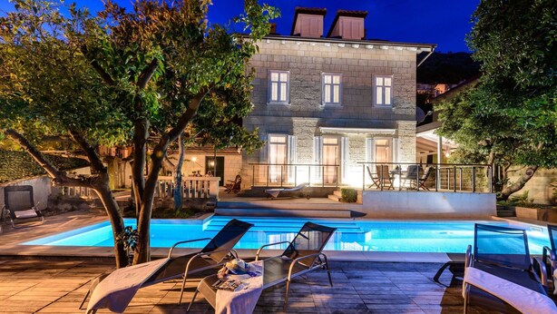 A poolside area with lounge chairs and a stone building in the background. - Villa Donna Paola (Dubrovnik)
