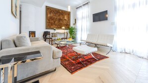 A modern living room with a sofa, a glass coffee table, a red rug, a white chair, and a large painting on the wall. - Villa Donna Paola (Dubrovnik)