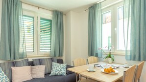 A cozy room with a sofa, a dining table, and a window with curtains. - Apartment Colette (Dubrovnik)