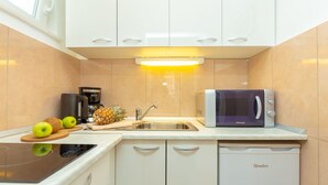 A compact kitchen with a microwave, sink, and a dishwasher. There are apples and a pineapple on the counter. - Apartment Colette (Dubrovnik)