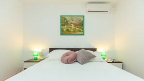 A neatly made bed with two pillows, a wall-mounted air conditioner, and a painting above it. - Apartment Colette (Dubrovnik)