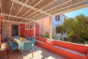 An outdoor patio with a table set for dining, surrounded by blue chairs, and a covered area with a thatched roof. - Hedera Estate, Villa Hedera XI (Dubrovnik)