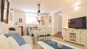 A well-lit living room with a sofa, dining table, chairs, a TV, and a chandelier. - Hedera Estate, Villa Hedera XI (Dubrovnik)
