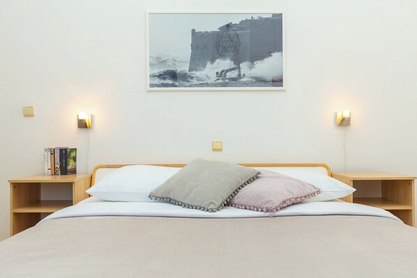 Une chambre à coucher avec un lit, des oreillers, des tables de chevet, un tableau accroché au mur et des appliques murales.