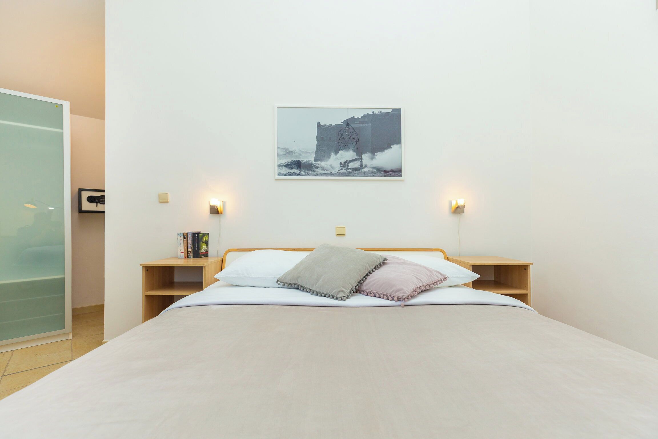 Ein Schlafzimmer mit einem Bett, Nachttischen, einem gerahmten Bild und Wandleuchten.