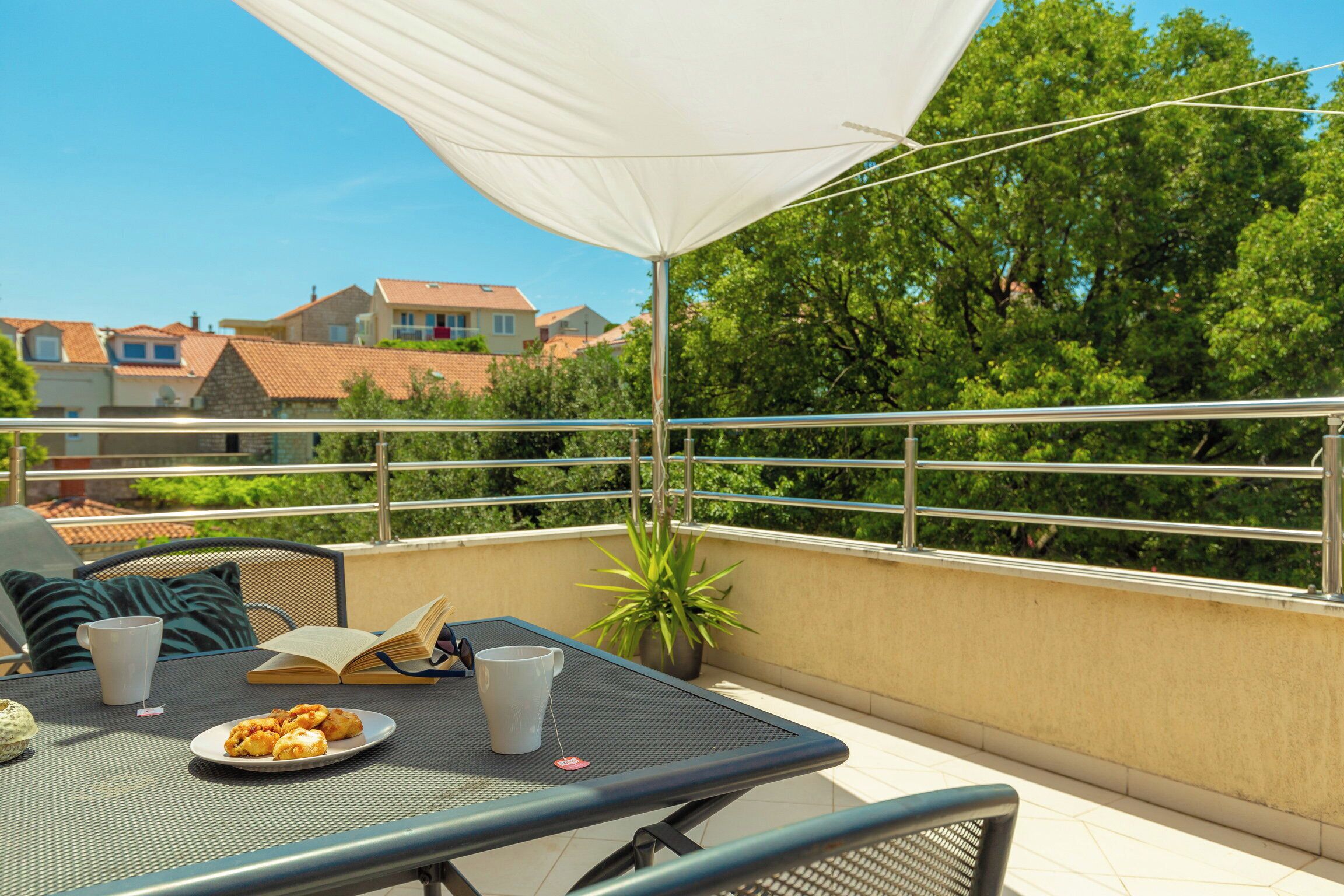 A balcony with a table, chairs, a potted plant, and a white umbrella.