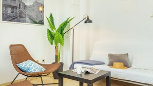 Ein Wohnzimmer mit Sofa, Sessel, Tisch, Stehlampe, Topfpflanze und Wandleuchte.