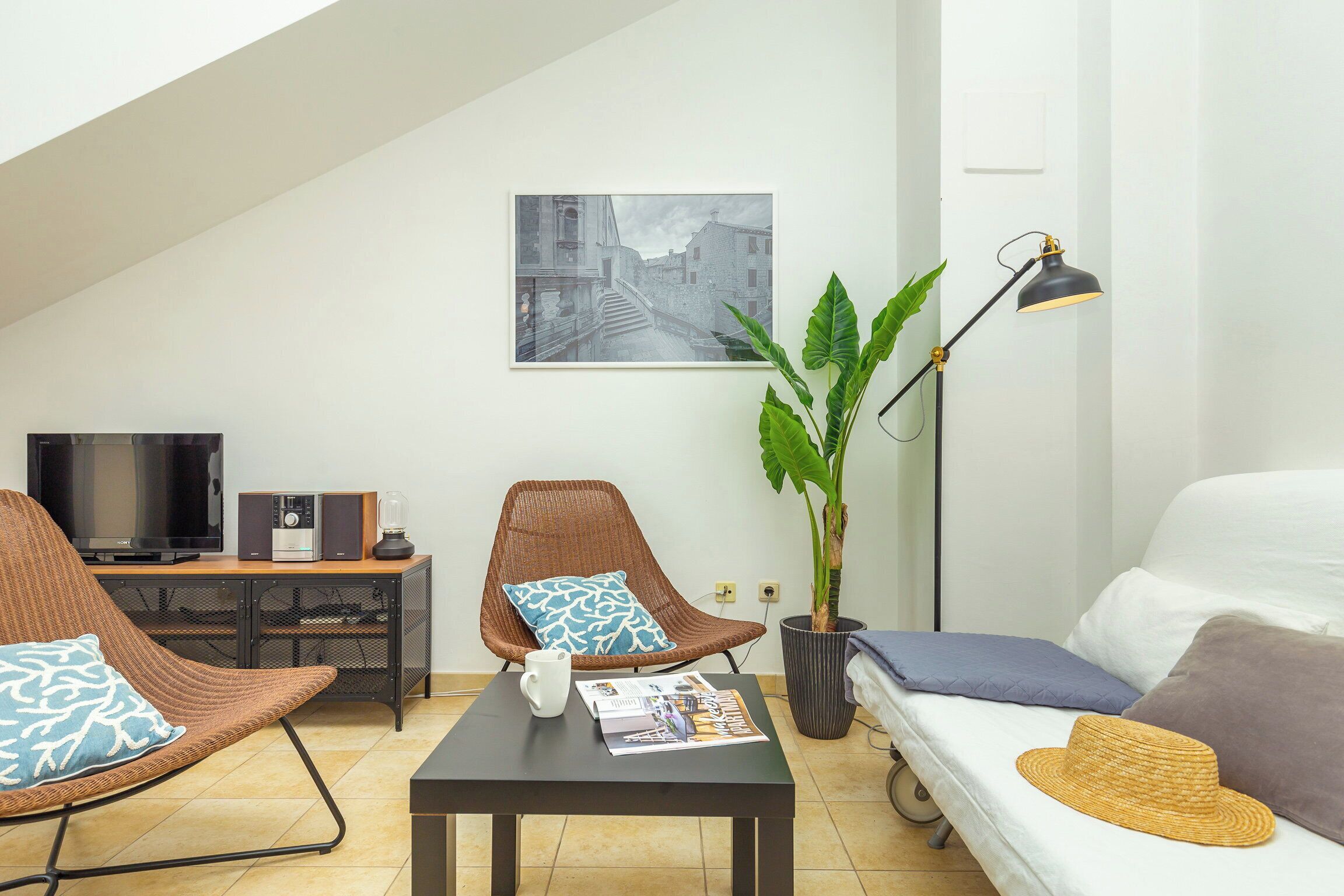 A modern living room with a TV, speakers, a dining table, a sofa, and a large plant.