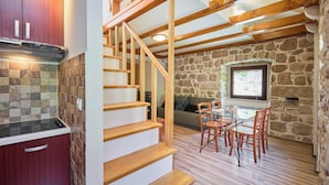 A kitchen with wooden cabinets, a stone wall, a dining area with a table and chairs, and a staircase. - Hedera Estate, Hedera A20 Apartment (Dubrovnik)