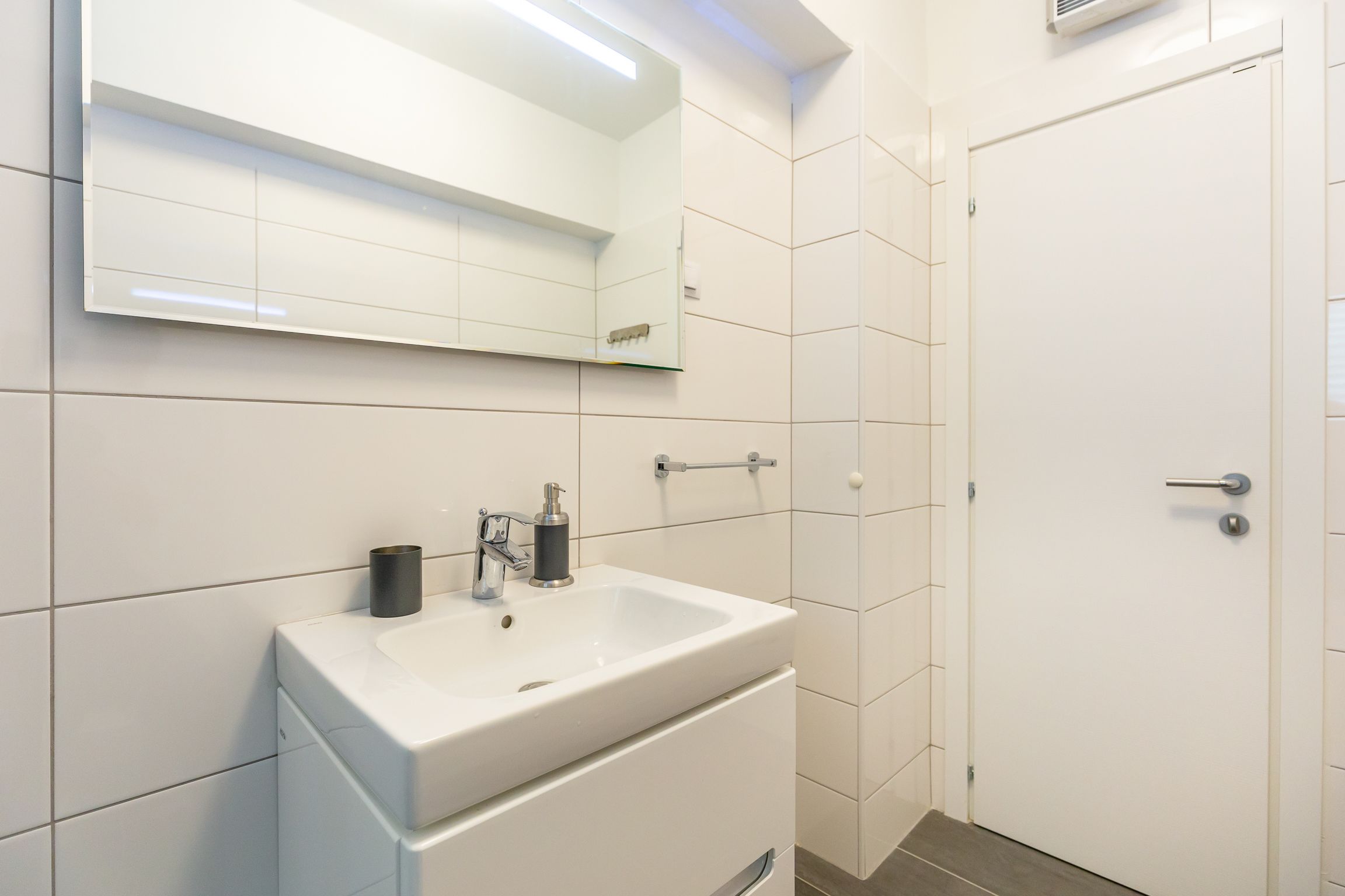 A modern bathroom with a white sink, mirror, and door.