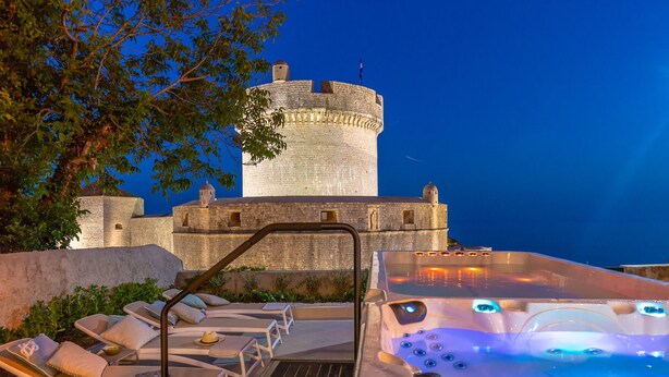 A castle-like structure with a round tower, outdoor lounge chairs, and a hot tub with illuminated jets. - Hedera Estate, Villa Hedera V (Dubrovnik)