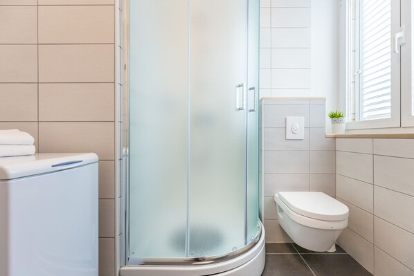 A modern bathroom with a glass-enclosed shower, a toilet, and a small window with blinds.