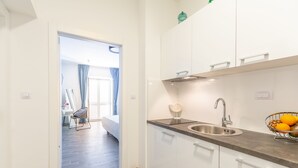 A modern kitchen with white cabinets, a stainless steel sink, and a countertop with a fruit bowl. - Hedera Estate, Villa Hedera V (Dubrovnik)