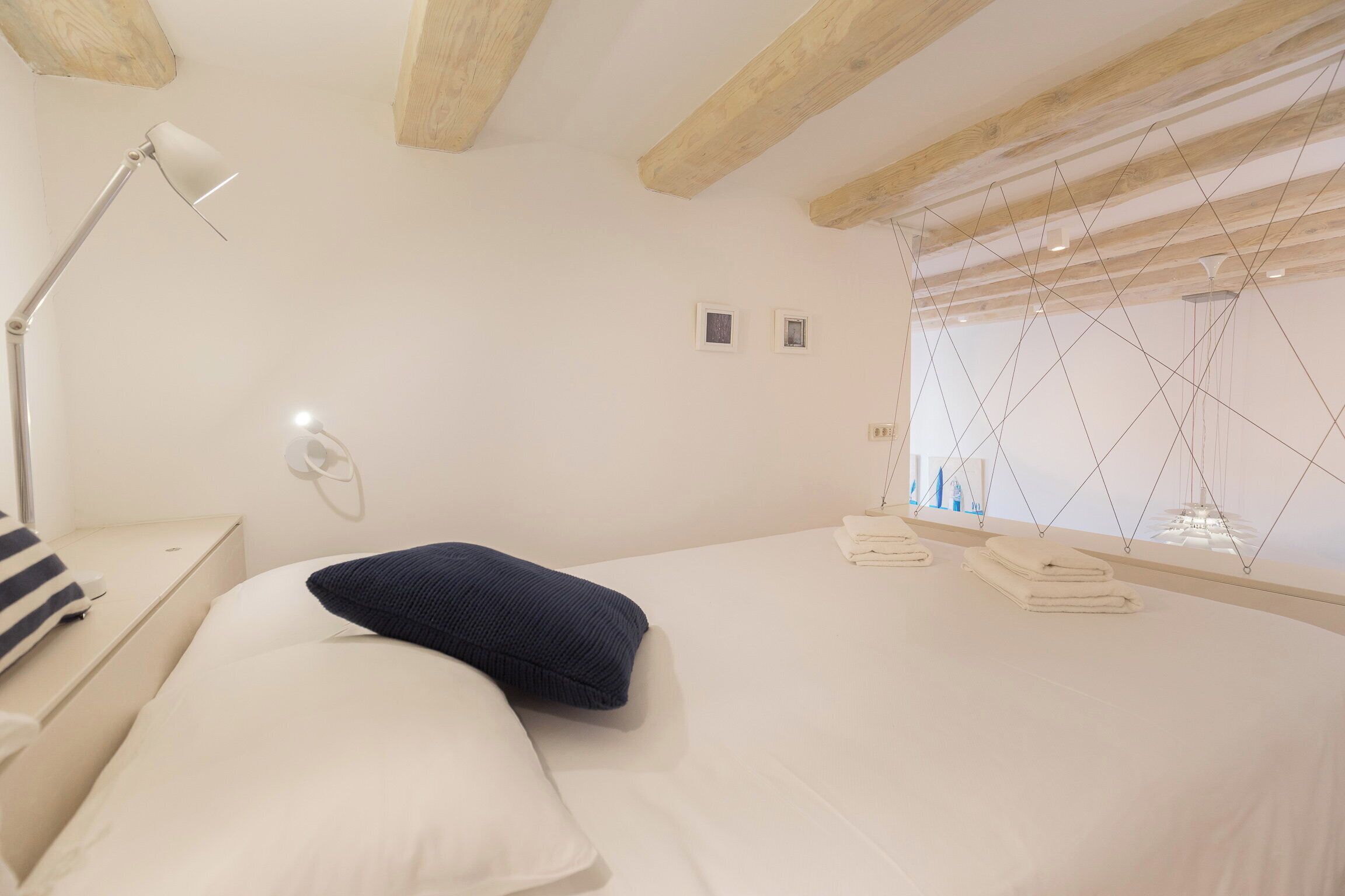 A bedroom with a bed, pillows, a bedside table with a lamp, and a window with blinds.