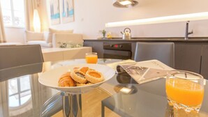 A breakfast setting with croissants, a glass of orange juice, and a menu on a glass table in a modern kitchen and living area. - Hedera Estate, Hedera A4 (Dubrovnik)