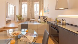 A modern kitchen with a dining area, a sofa, and a bed in a bright room with large windows. - Hedera Estate, Hedera A4 (Dubrovnik)