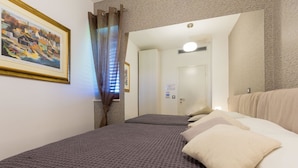 Ett hotellrum med två sängar, en tavla på väggen och en dörr som leder till ett annat rum.