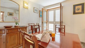 A dining area with a wooden table, chairs, a book, a glass of orange juice, and a large mirror. - Hedera Estate, Hedera A17 (Dubrovnik)