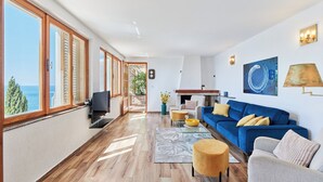 A spacious living room with a large blue sofa, a television, and a view of the sea through large windows. - Hedera Estate, Hedera A17 (Dubrovnik)